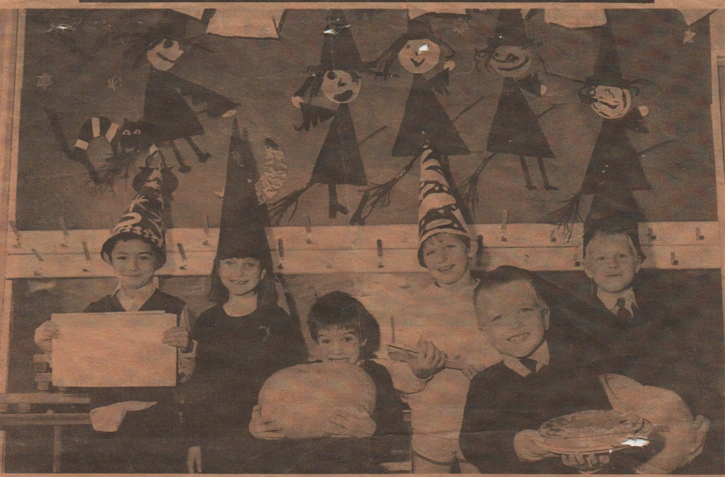 Scan of a newspaper photo. Several infants stand in front of a Halloween display.