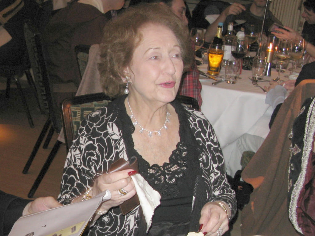 An older woman with curly hair, wearing a black and white dress.