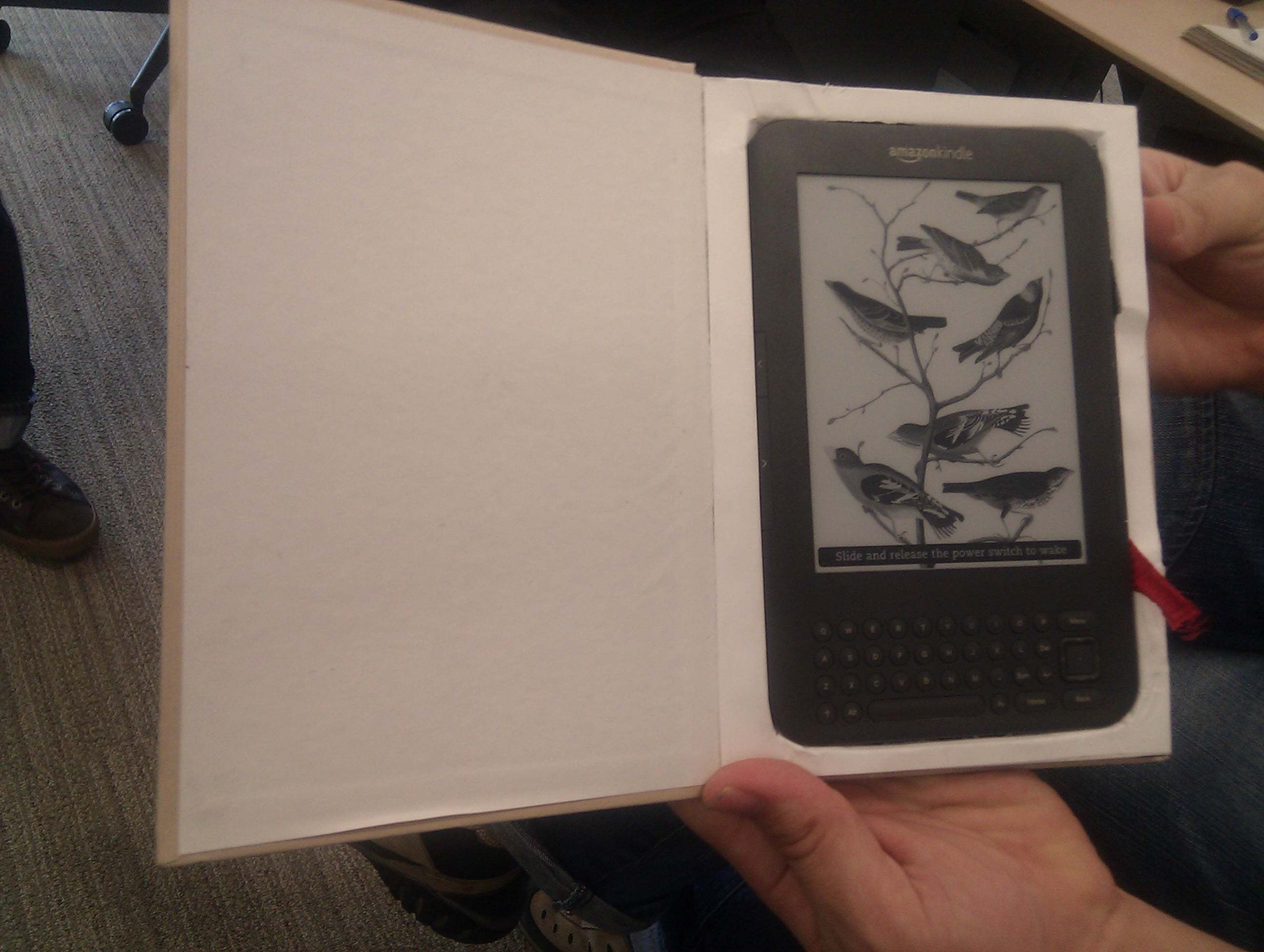 A Kindle nestled in a hollowed out paper book.