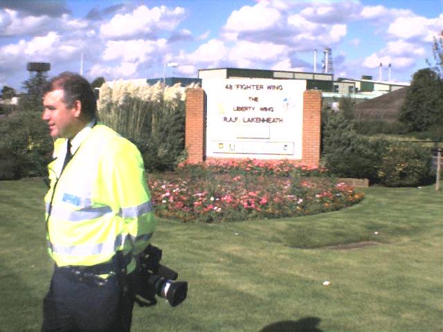 A police office looks away. He is carrying a large camera.