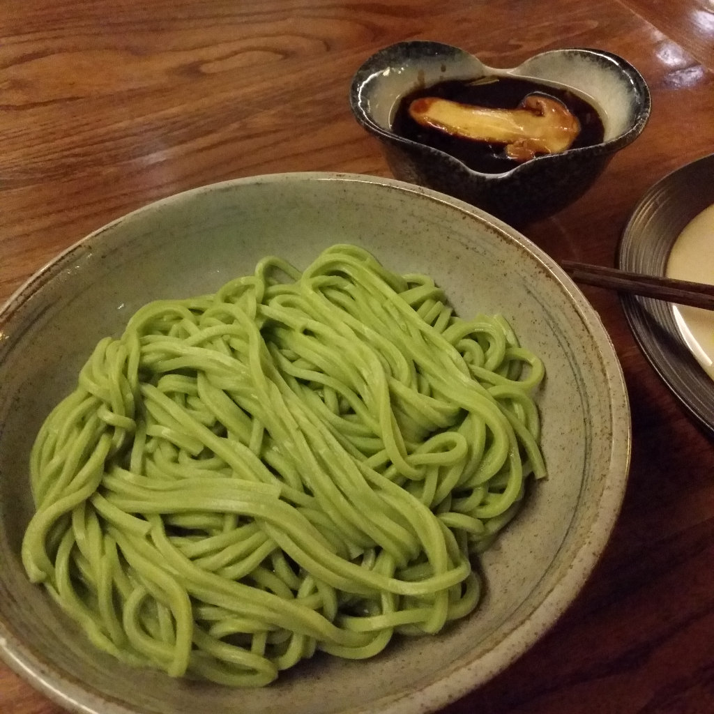 Bright green noodles with a separate bowl of gravy. A single slice of mushroom floats in it.