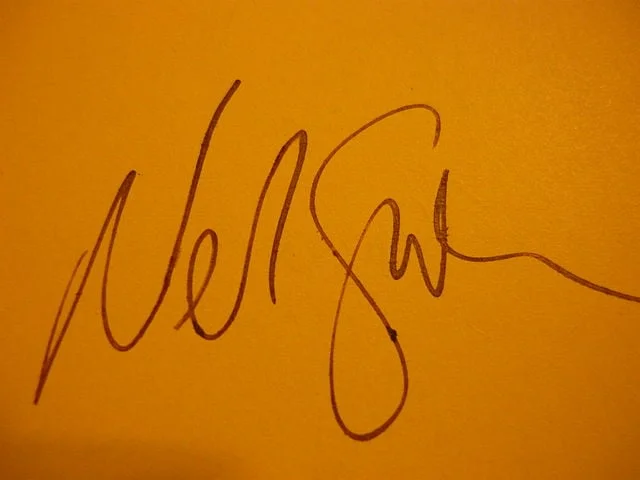 Neil Gaiman's autograph, scrawled on orange paper.