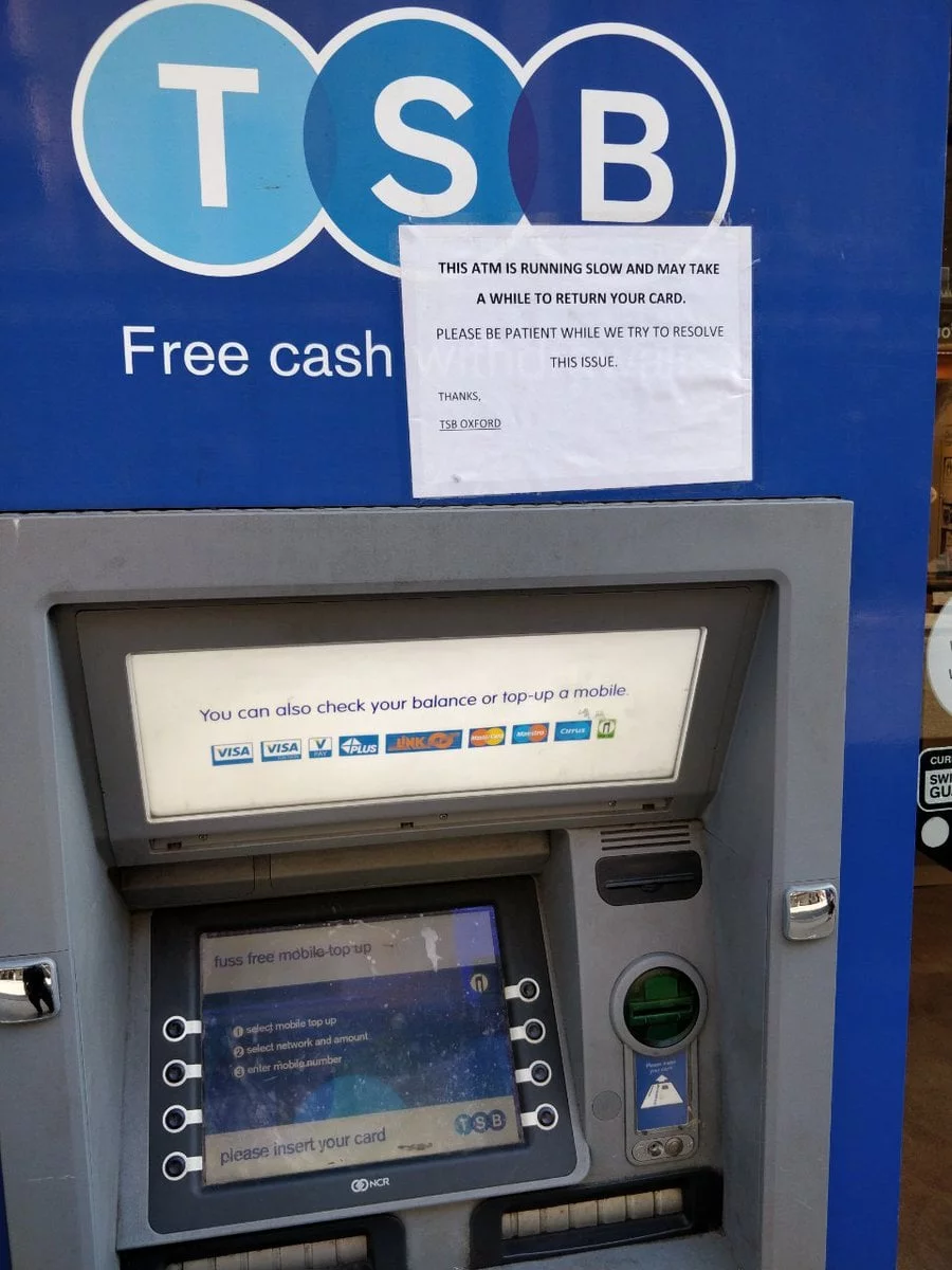 A sign is taped haphazardly to an ATM. It warns people that the ATM is slow and may take a while to return their card. There is no branding on the sign. 