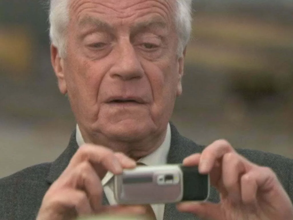 Old white actor holding a phone.