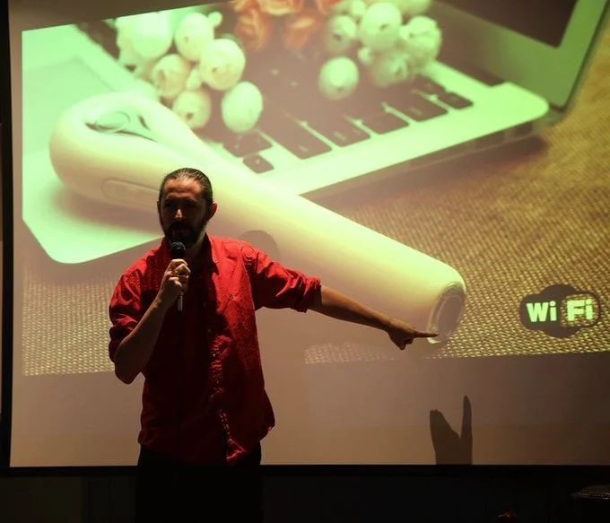 Terence Eden performing stand u comedy. He is holding a microphone.