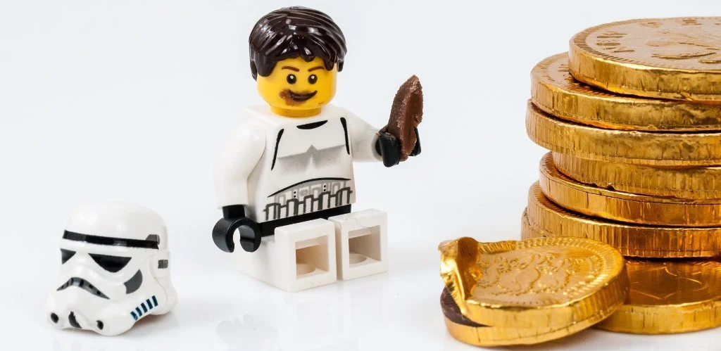 A tiny lego Storm Trooper eats a chocolate coin.