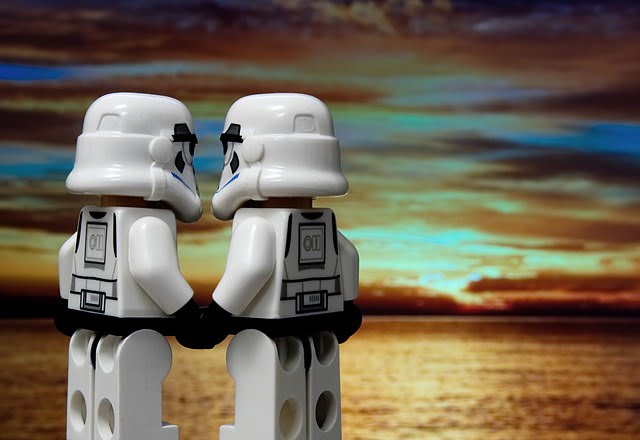 Two little Lego Stormtroopers hold hands in front of a sunset.