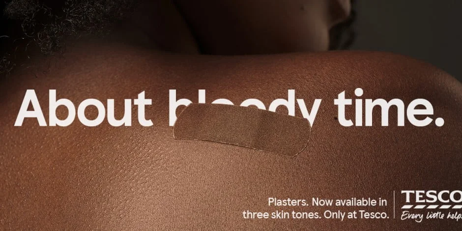 The words "about bloody time" written on brown skin. The word bloody is partially obscured by a sticking plaster the same colour as the skin.