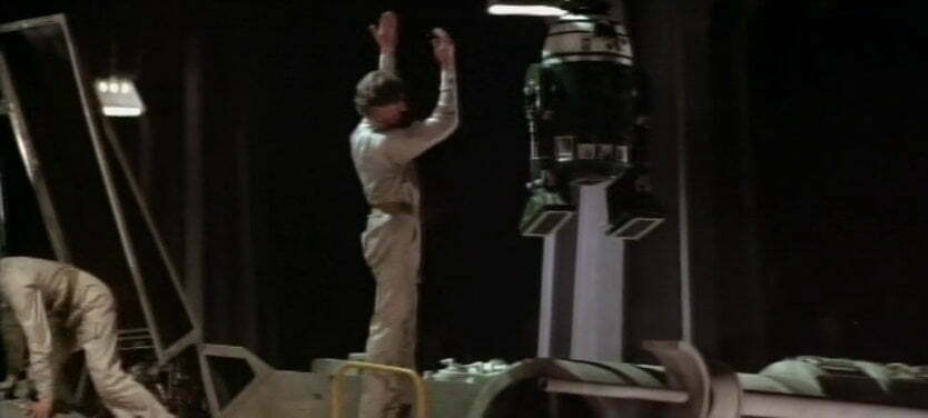 Green droid being lowered into a spaceship.