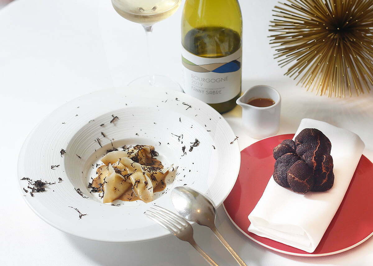 Photo of a play of pasta, black truffle shavings, and white wine.