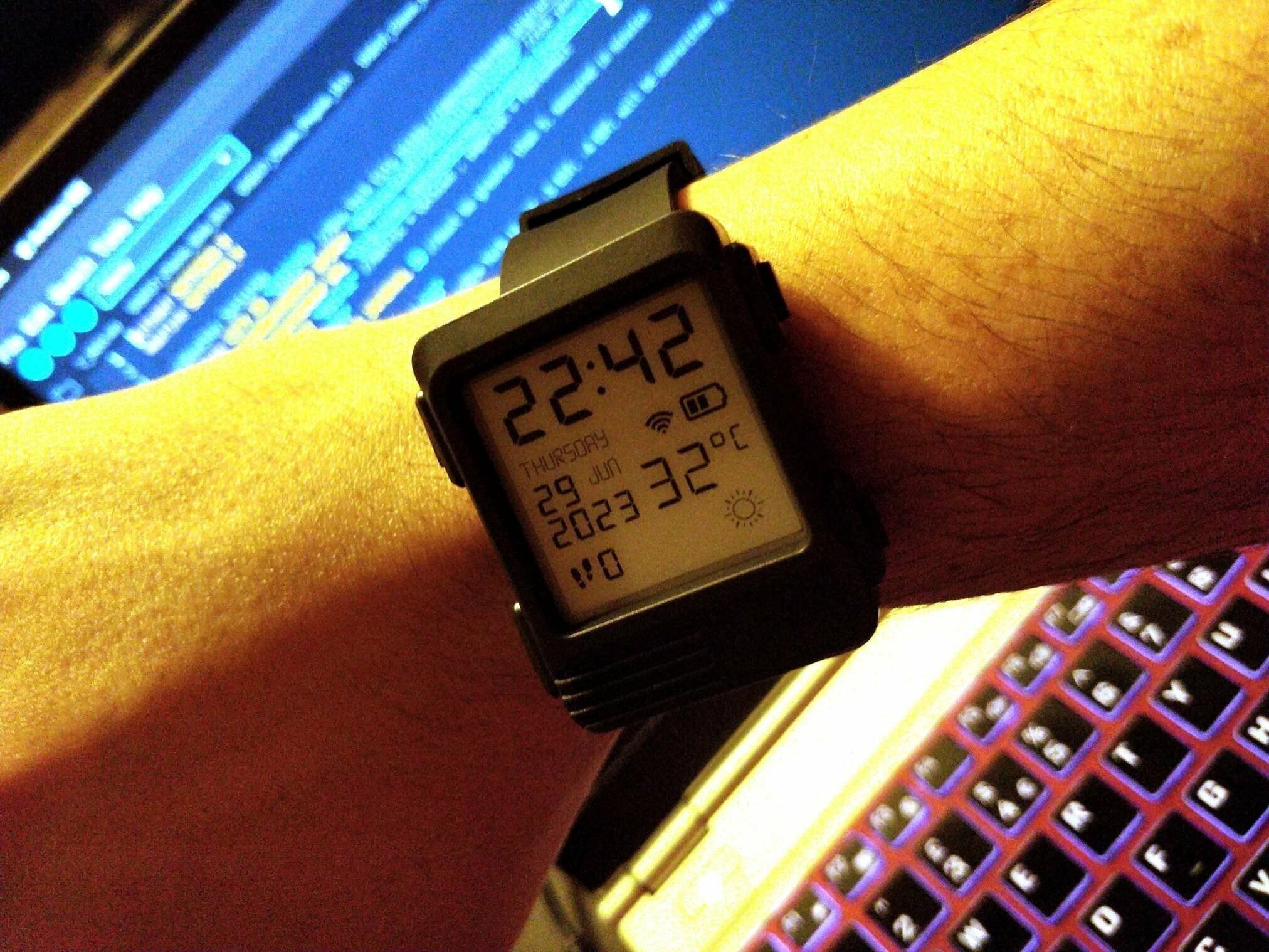 A watch showing the correct time. There is some blurred code on the computer screen behind it.