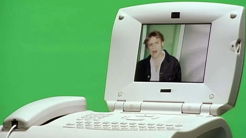 A white plastic desktop phone with QWERTY keyboard and a video screen.