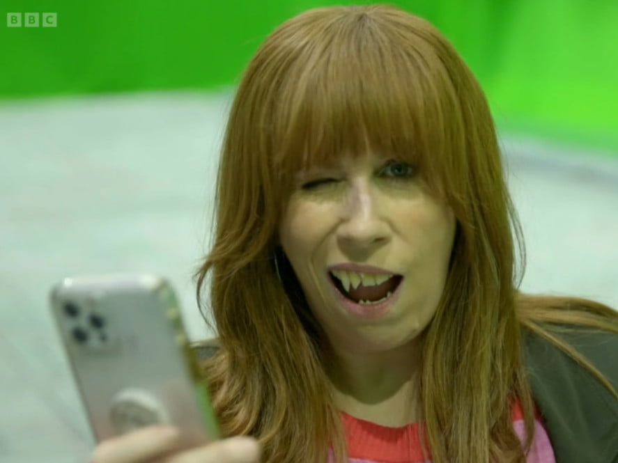 Catherine Tate holding a phone while wearing scary teeth.