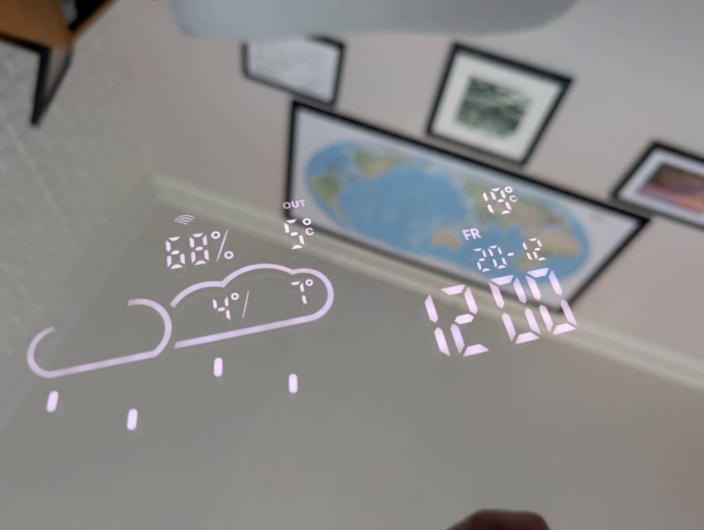 Mirrored surface with white writing on it. It shows the time, date, and weather conditions.