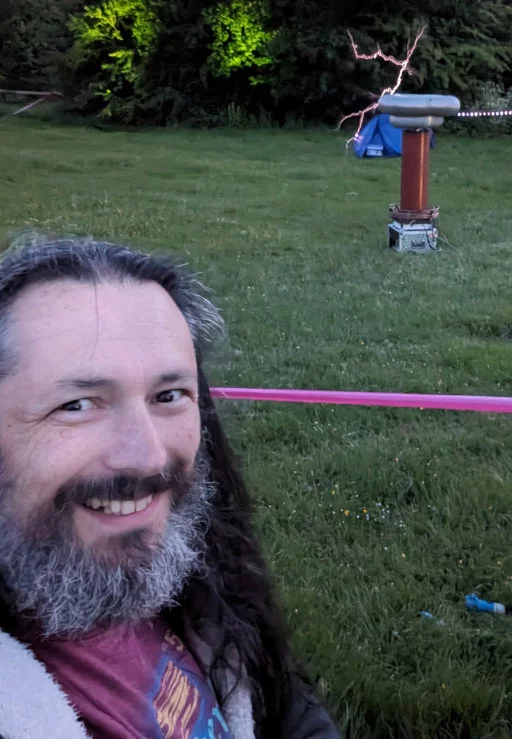 Selfie of me in front of a Tesla Coil. A big metal tube shooting sparks.