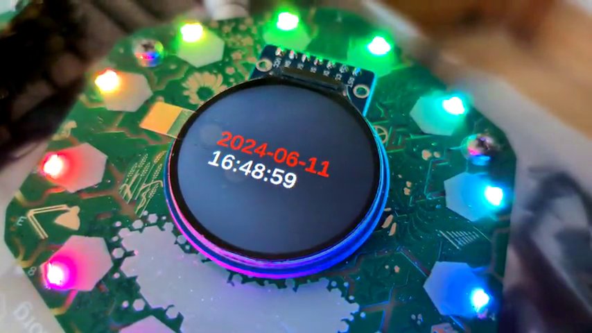 Hexagonal circuit board with circular screen. It is showing the date and time.