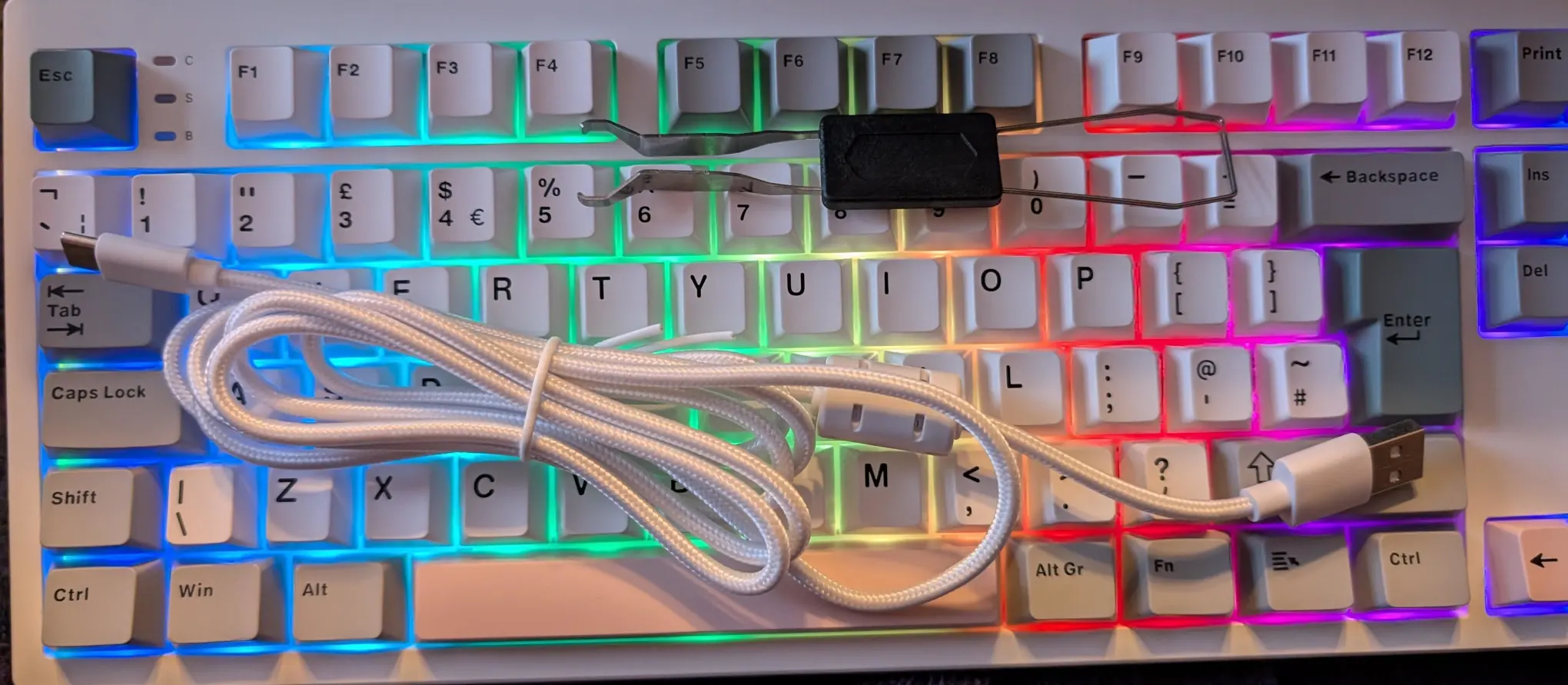 A brightly multicoloured mess of a keyboard with a USB cable and keytool on it.