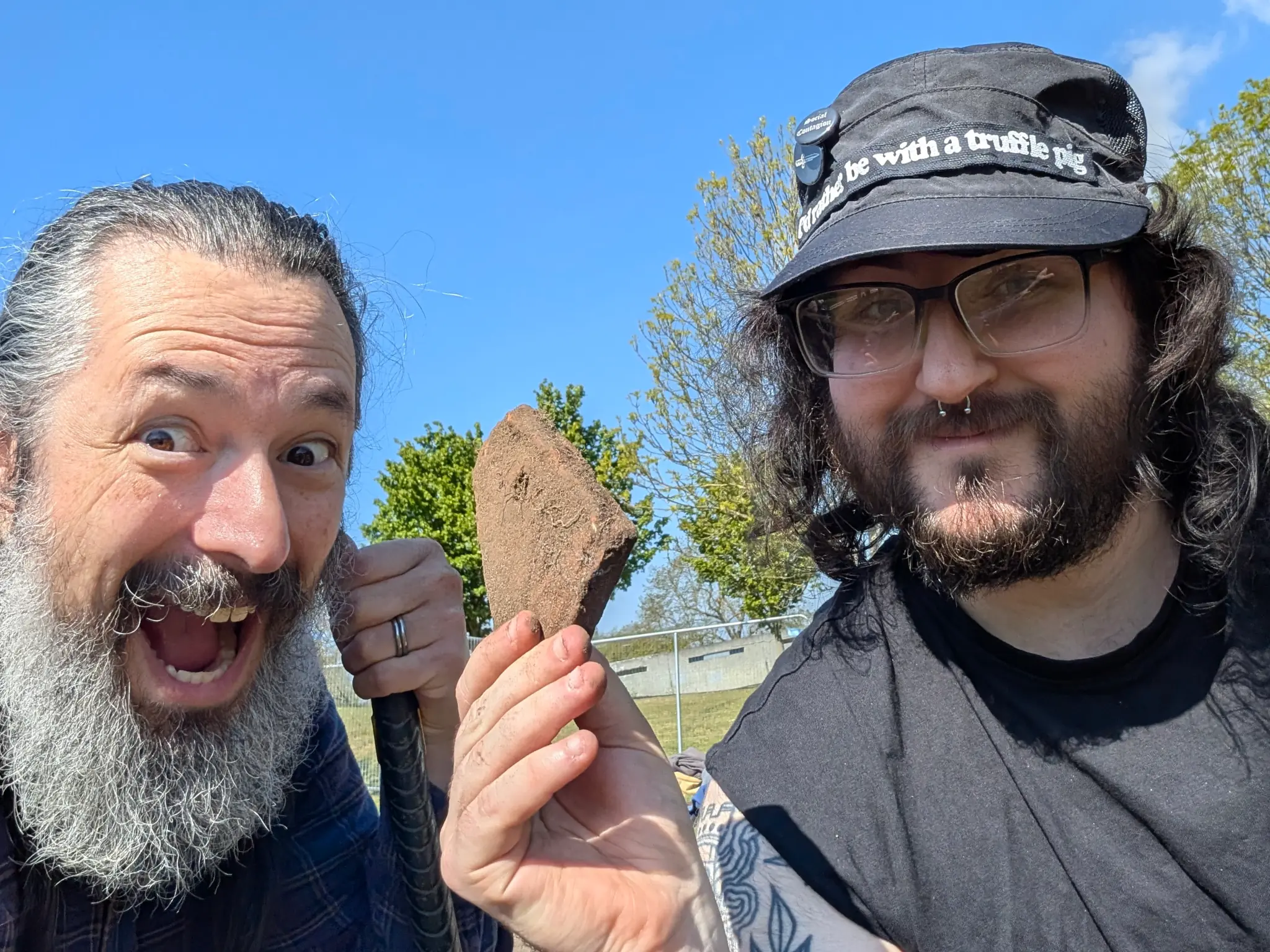 Two grinning buffoons hold up a bit of old tile.