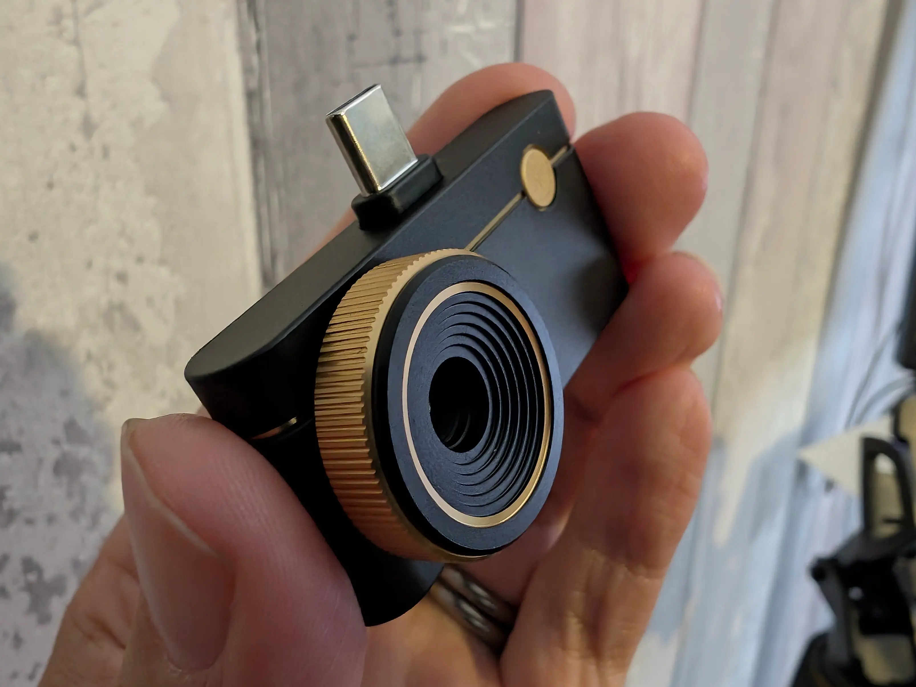 A small black camera with gold accents. It is held in the fingertips.