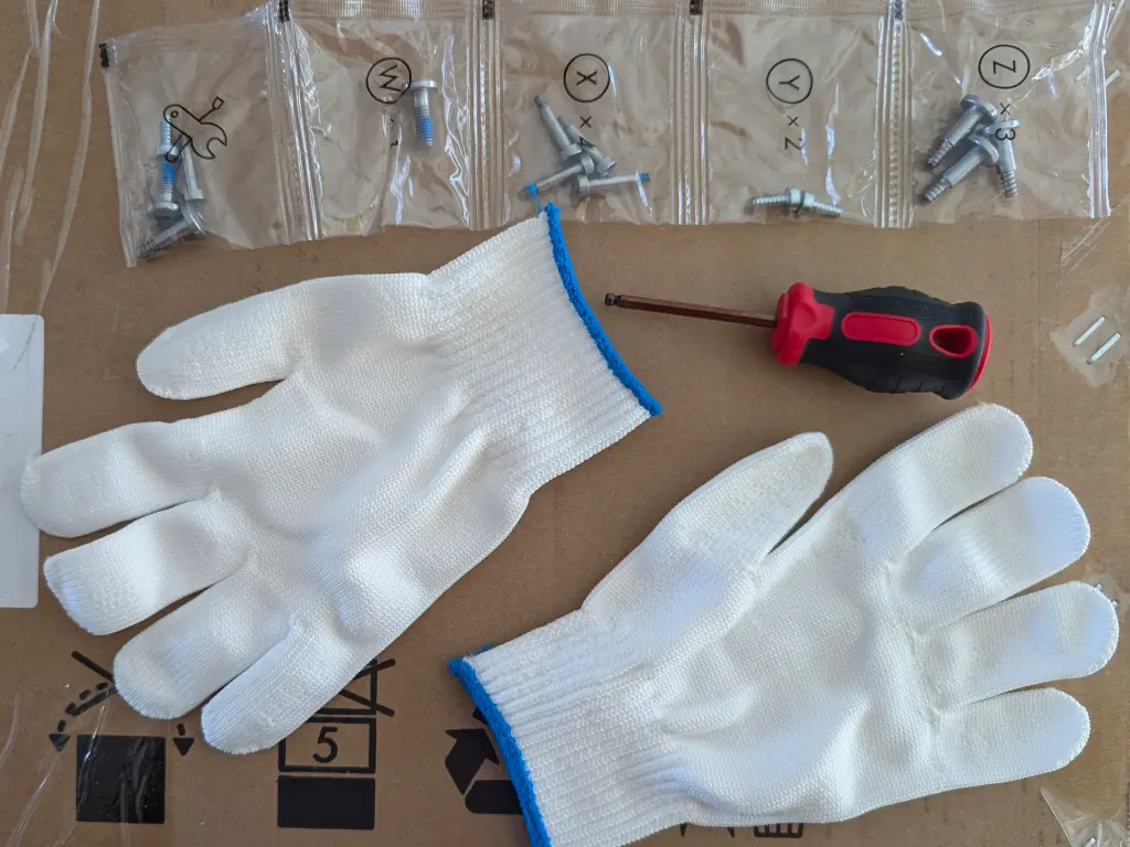 Screws in labelled pouches, a driver, and a pair of white gloves.