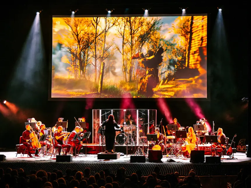 Photo of an orchestra playing in front of a large screen showing game footage.
